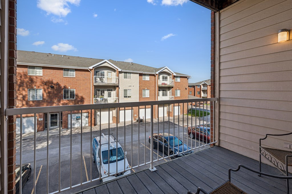 A balcony with a metal railing and a few cars parked in the parking lot.
