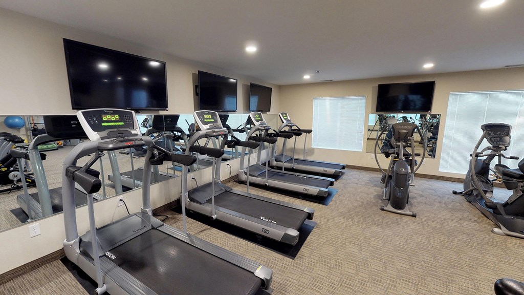 a gym with cardio equipment and flat screen televisions