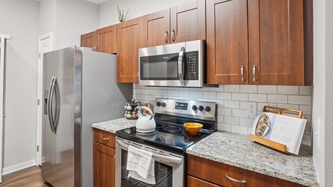 A kitchen with a refrigerator, microwave, oven, and a stove top.