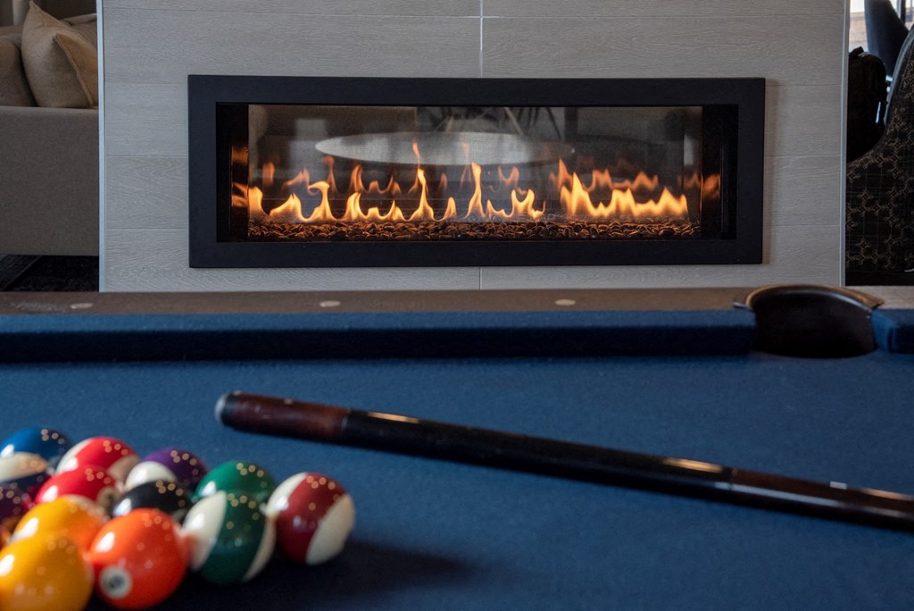 Pool table, with balls and stick in the foreground, fireplace in the background