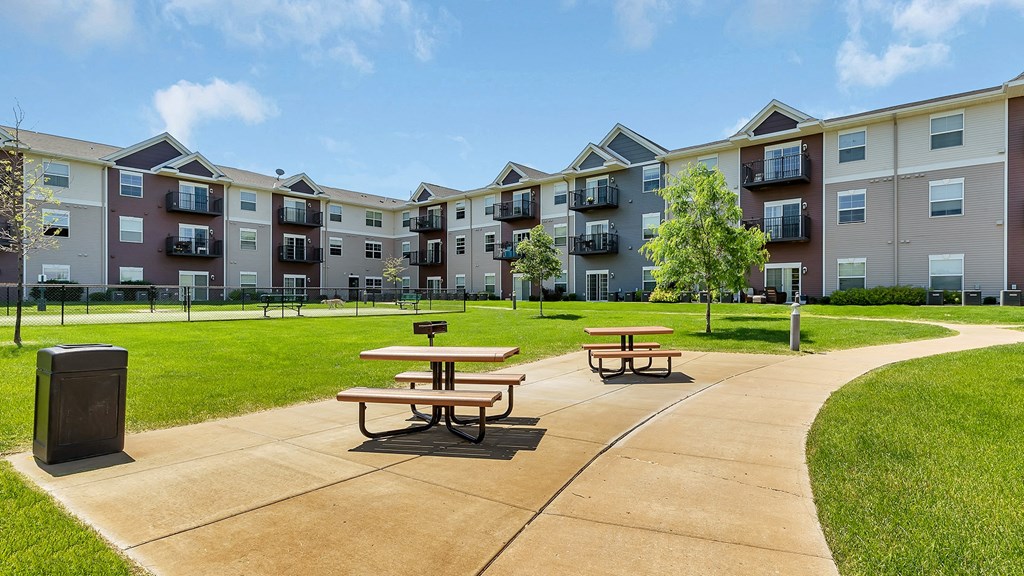 an outdoor patio with picnic tables in front of an apartment building
