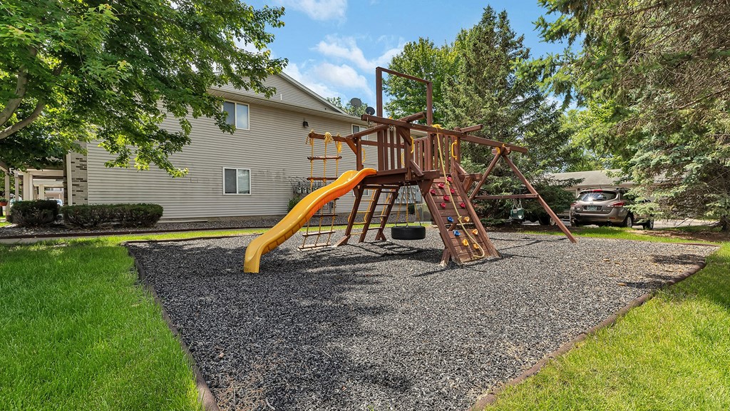 a swing set with a yellow slide in a backyard