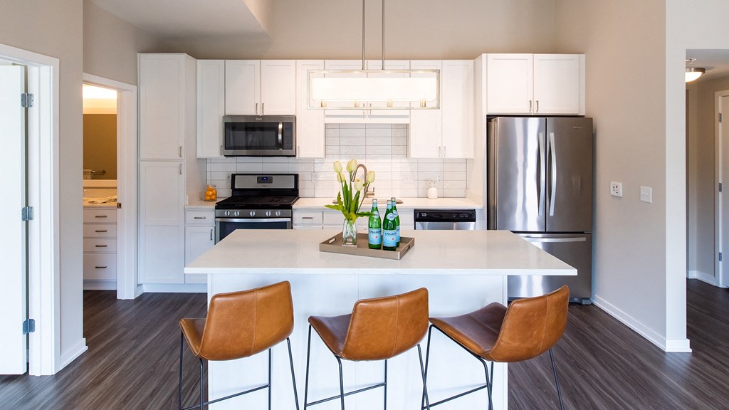 a kitchen with white cabinets and a white island with three chairs