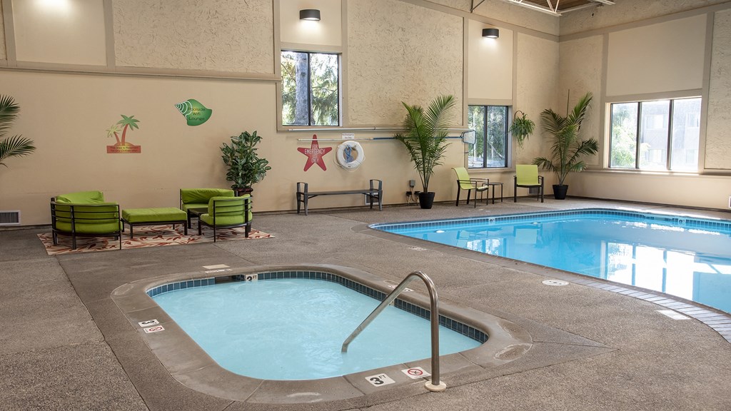 a swimming pool with a hot tub in the middle of a room with green chairs and plants