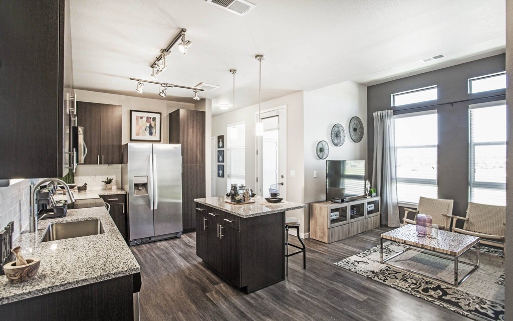 Open kitchen and living room with small center island, dark wood cabinets and granite countertops, furnished living room space