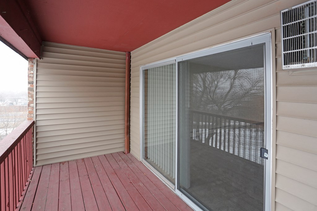 Outdoor private balcony with wood railing and sliding glass door leading inside