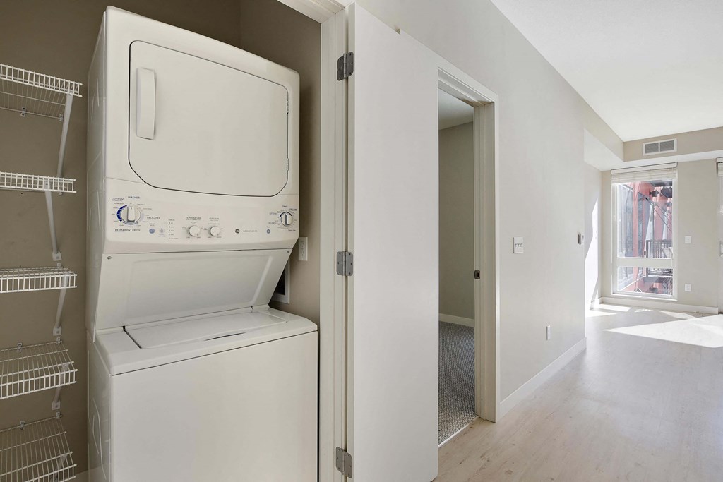 In unit stacked washer dryer in convenient closet with shelf storage on the left of the washer/dryer.