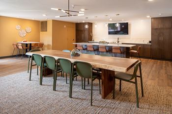 Community room with large wooden table, full kitchen and island with barstools and mounted TV