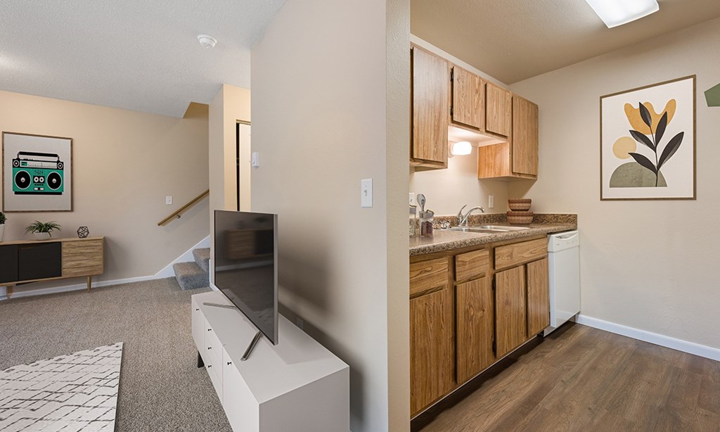A modern living room with a flat screen TV and a kitchen area with wooden cabinets.