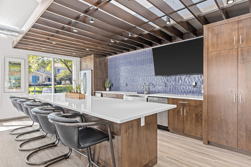 A modern kitchen with a long white island and black chairs.