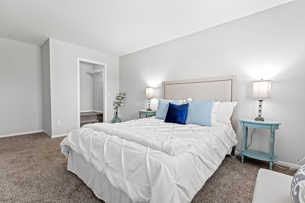 A bedroom with a large bed and a small table with a lamp.