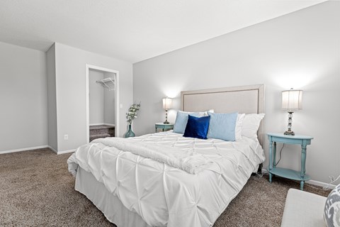 A bedroom with a large bed and a small table with a lamp.
