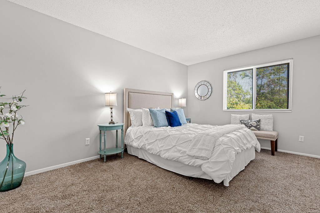 A bedroom with a large bed, a nightstand with a lamp, and a vase with flowers.