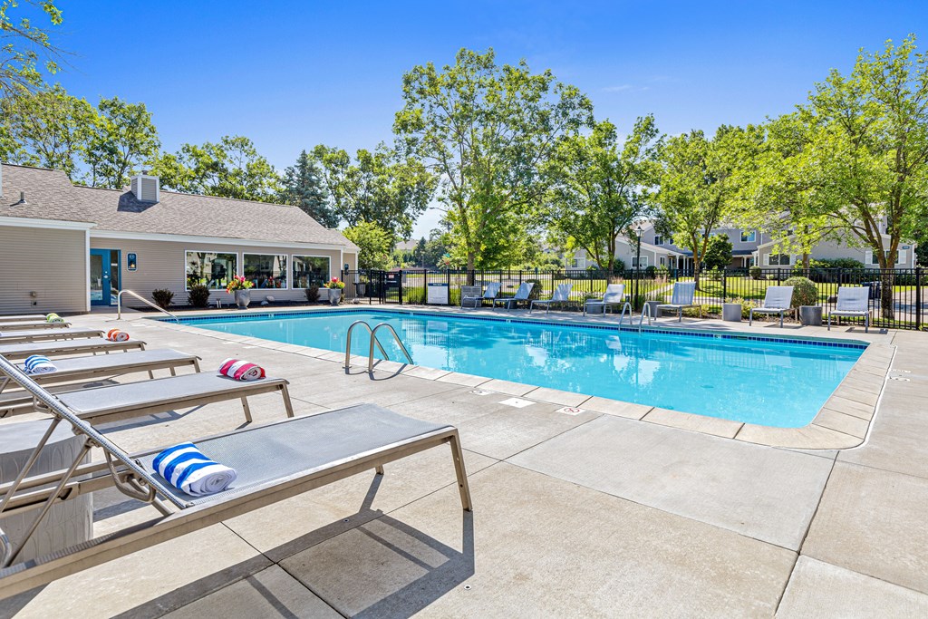 A pool with sun loungers and a house in the background.