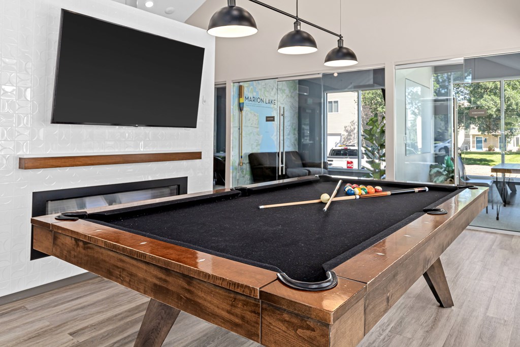 A pool table with a black cloth and a television mounted on the wall.