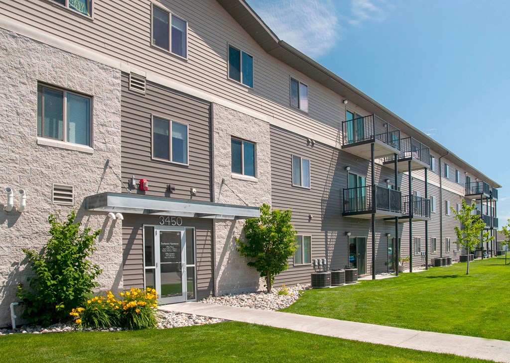 Exterior of Southpoint Apartments featuring grass lined sidewalk leading to the building. View of building showcases many windows and balconies lending ample natural light to the units.