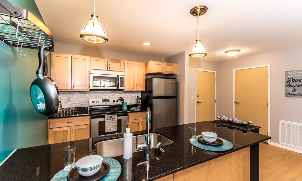 Bright and spacious kitchen with stainless steel appliances, pendant lighting above the island, and pan rack on the left side to hang pots and pans.