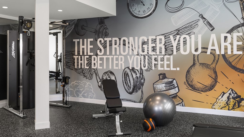 a fitness room with a gym chair and a wall with a motivational quote on it