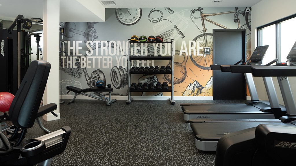 a gym with cardio equipment and a wall mural of the strength you are better you