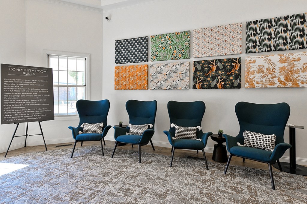 four blue chairs in a room with a wall filled with different colored canvases