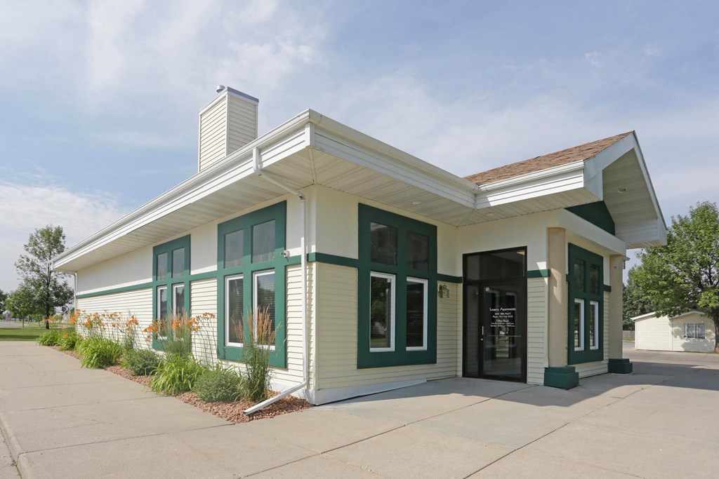 Exterior of The Legacy Leasing Office with green trim windows and shrubbery lining the sidewalk.
