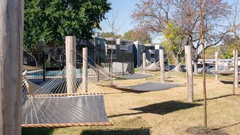 a playground with hammocks and a fence and houses in the background at The Bosk Apartment Homes, Woodbury, 55125