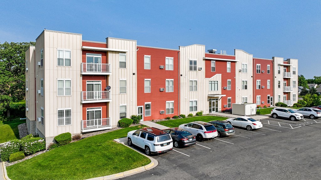 an exterior view of an apartment building with cars parked in a parking lot