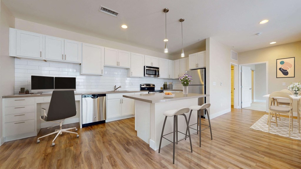 Spacious modern kitchen with white cabinetry, stainless steel appliances, and pendant lighting above the island. Kitchen opens up into separate dining area.