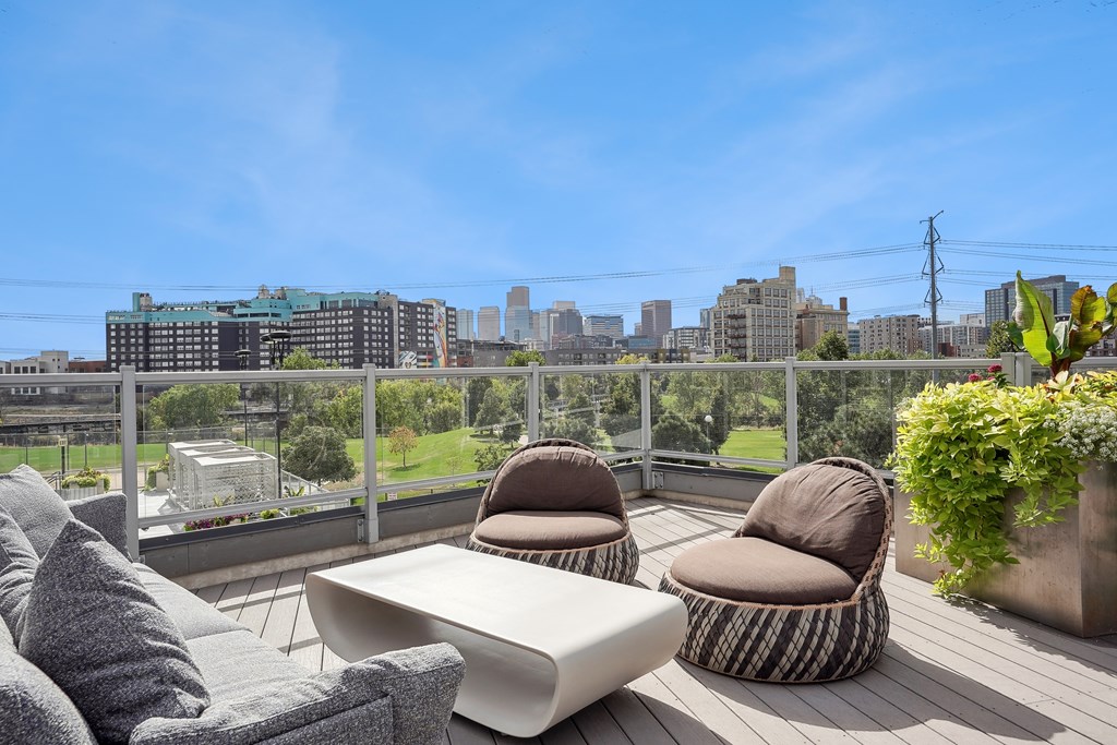 A balcony with a couch, chair and table with a city view in the background.