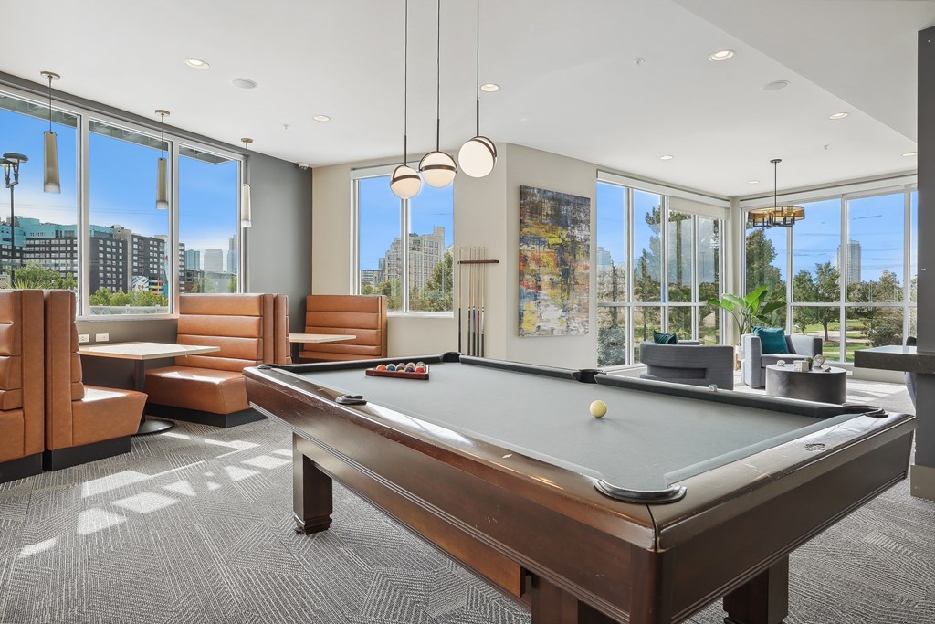 A pool table is in the middle of a room with leather chairs and a view of the city.