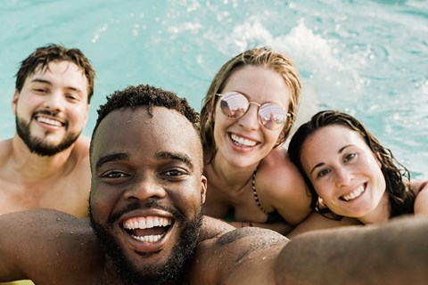 Four people are smiling and taking a selfie in a pool.