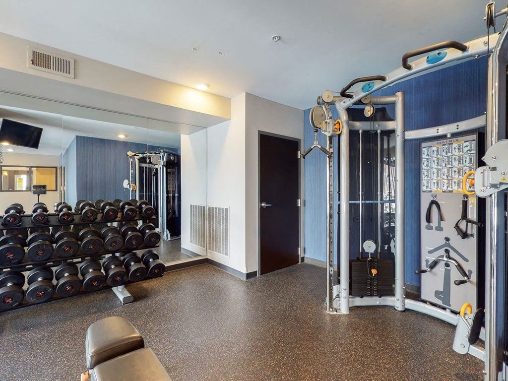 Fitness Center with hard rubber flooring, strength cable machine and dumbbell rack with mirror behind