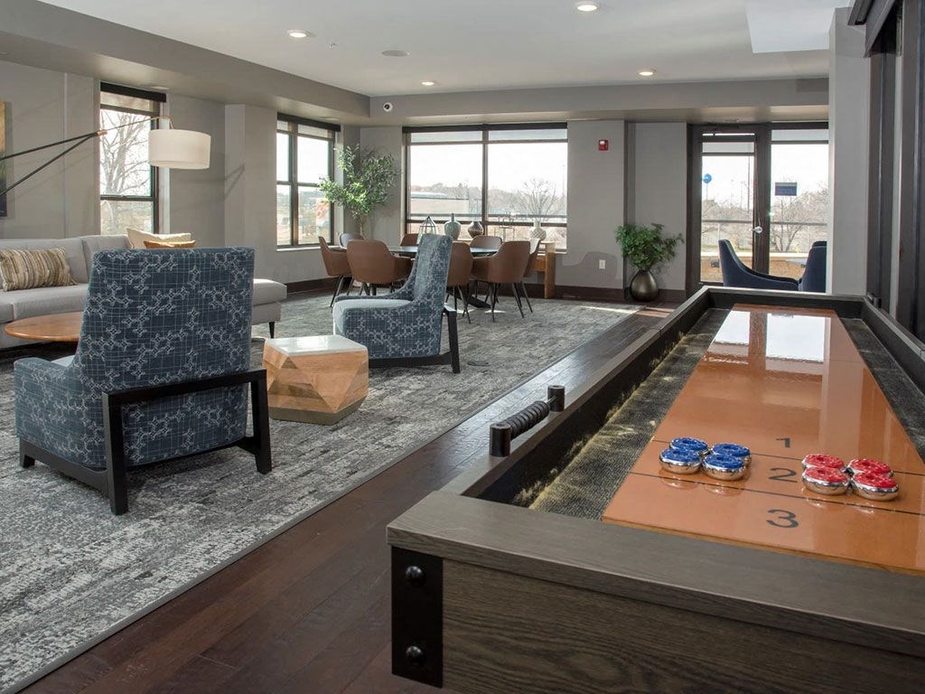 Community room with large circular table and many chairs, shuffleboard table