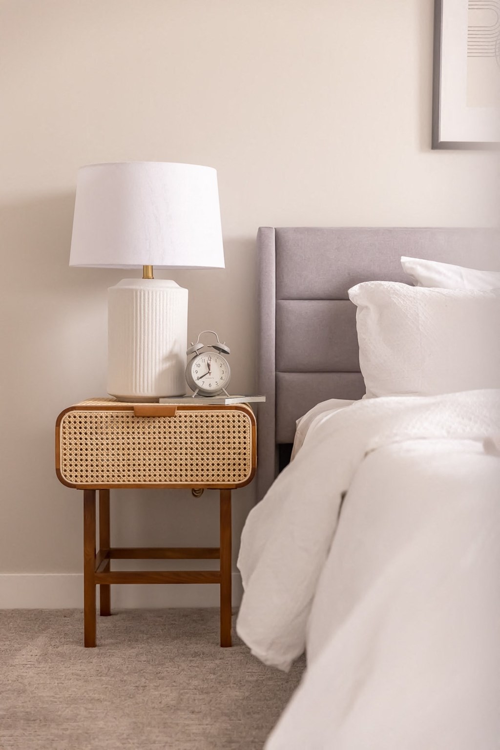 a nightstand with a lamp and a clock on it next to a bed