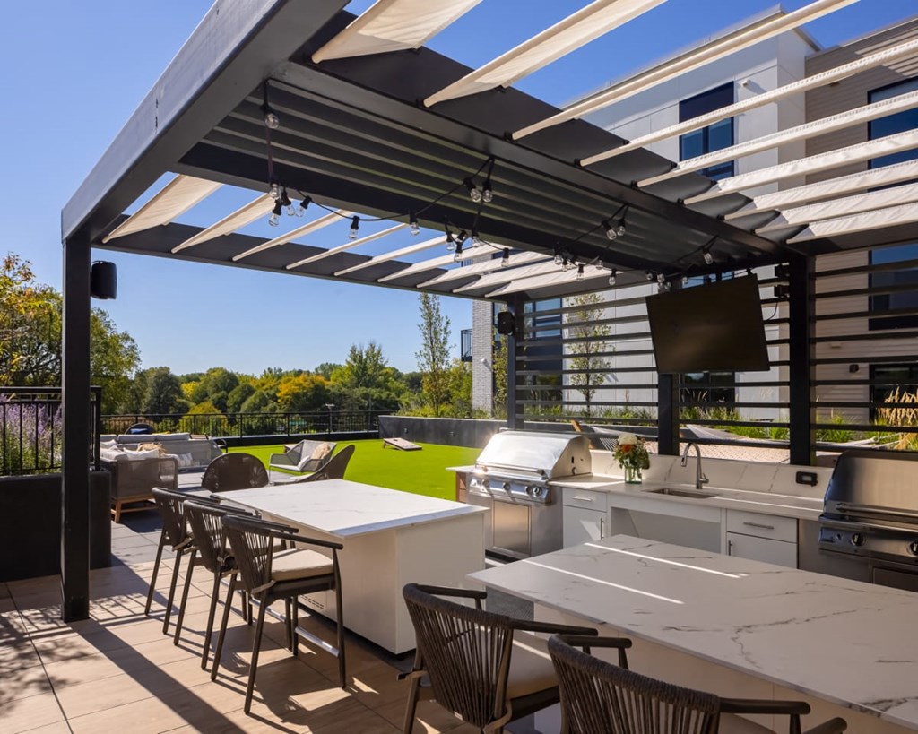 a pergola with white tables and chairs on a patio with a grill and a television