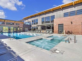 A large outdoor swimming pool with a hot tub and lounge chairs.