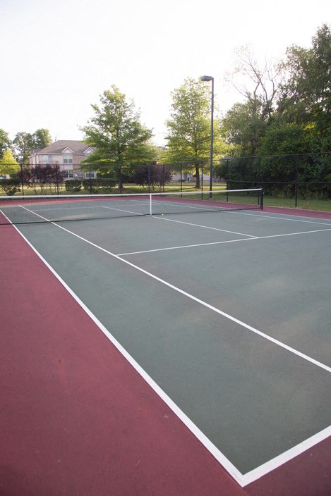 a tennis court with trees and a house in the background