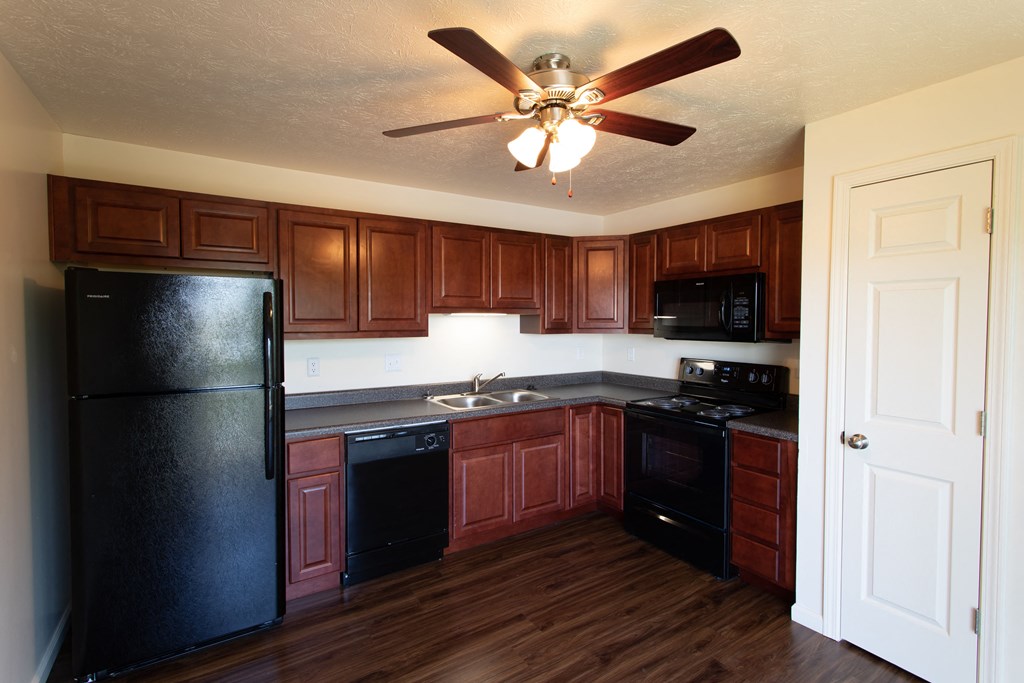 an empty kitchen with black appliances and a ceiling fan