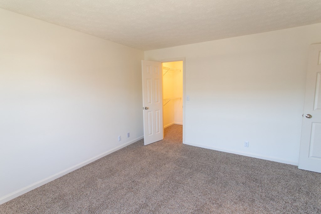 a bedroom with carpet and white walls and a door to a closet