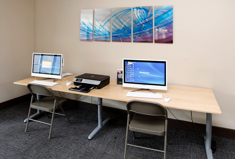two computers and a printer sit on a table in a room with two paintings on the wall