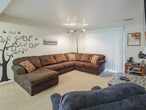 A living room with a large brown sectional sofa and a tree mural on the wall.