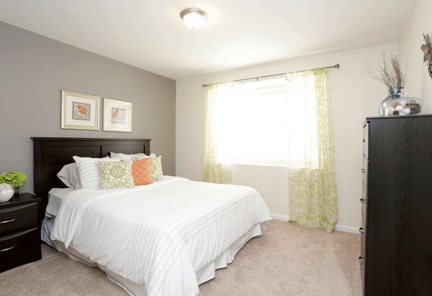 a bedroom with white bedding and green and orange pillows