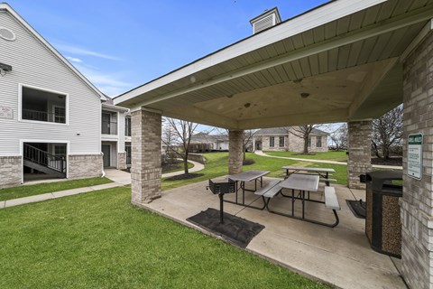A covered picnic area with tables and benches is situated in a grassy area.
