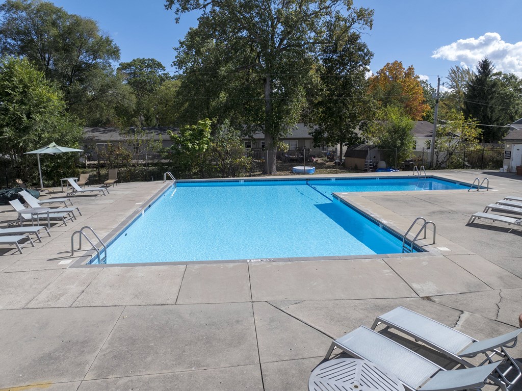 A large blue swimming pool surrounded by trees and chairs.