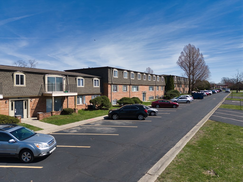 a row of apartment buildings with cars parked in a parking lot