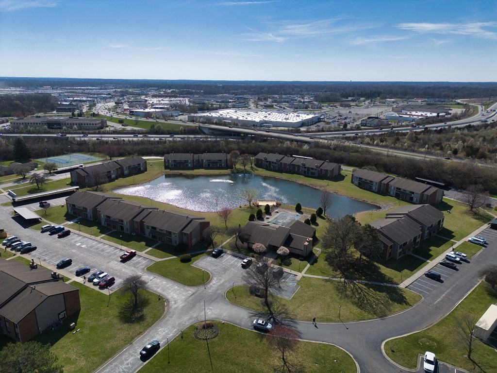 an aerial view of a pond in the middle of a neighborhood with houses and cars