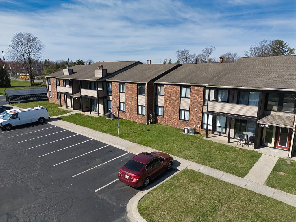 an apartment building with a red car parked in a parking lot
