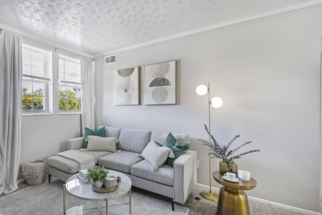 A living room with a grey couch, a glass table, and a gold floor lamp.