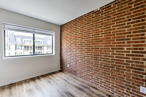 A room with a brick wall and a window overlooking a building.