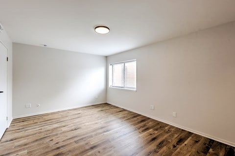 A room with wooden flooring and a window with blinds.